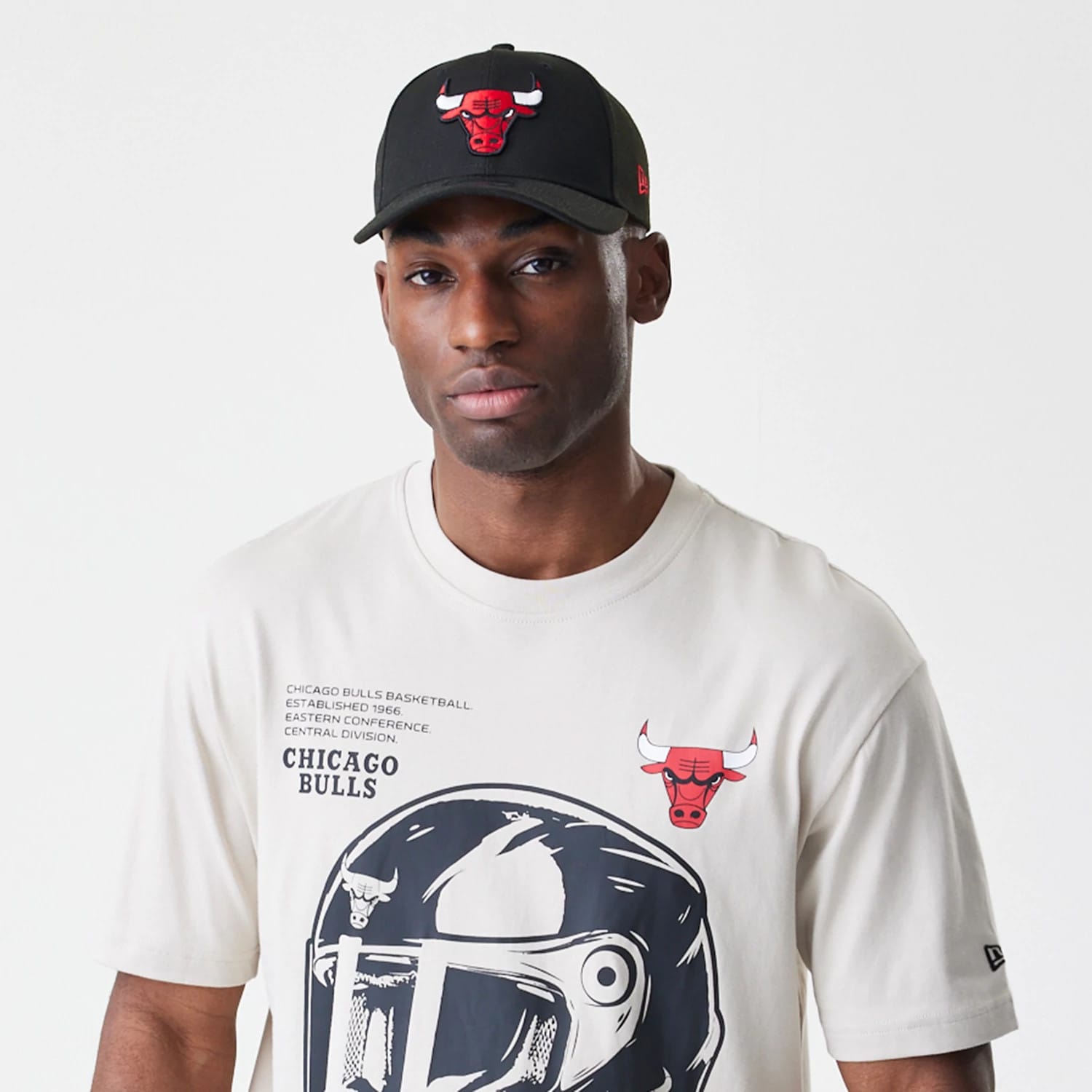 New Era Chicago Bulls Modern Driver Light Beige T-Shirt, on-model view showing the front graphic with a large helmet design, a red bull logo on the upper chest, and New Era logo on the left sleeve.