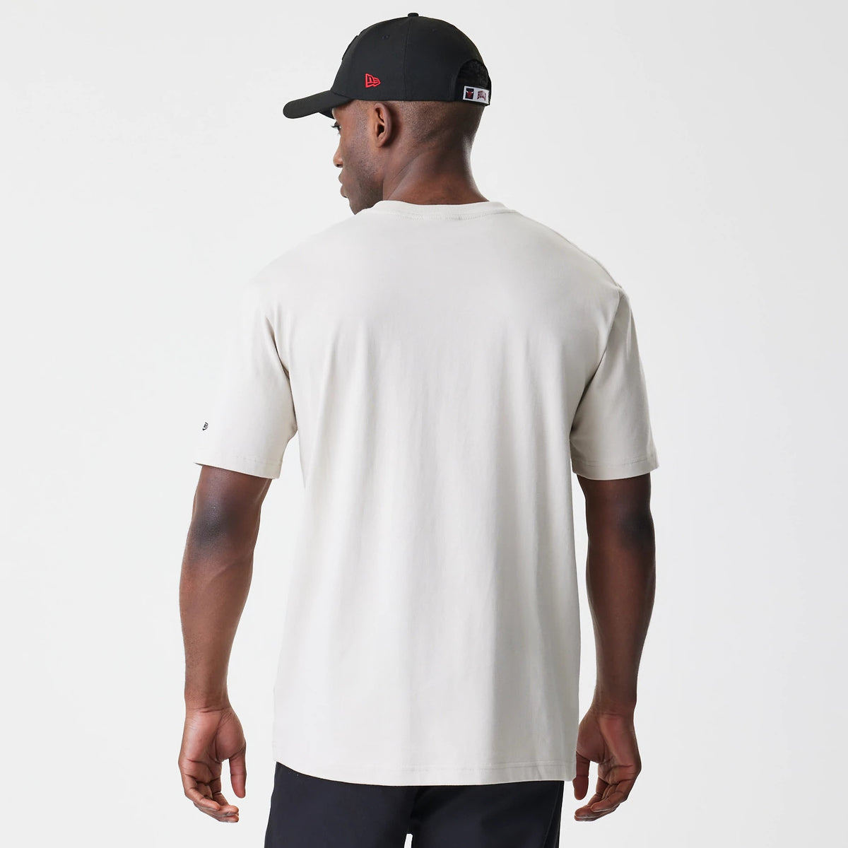 New Era Chicago Bulls Modern Driver Light Beige T-Shirt, rear view showing the plain light beige back panel with short sleeves, a small debossed logo on the left sleeve, worn by a person in a black cap.
