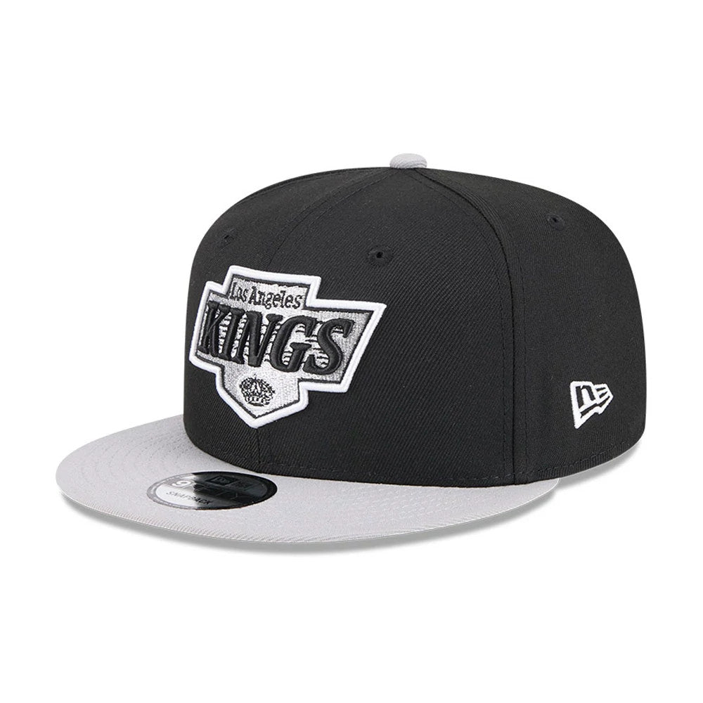 LA Kings NHL Evergreen Black New Era 9FIFTY Snapback Adjustable Cap, three-quarter view with raised white and black embroidered logo on the front panel, grey visor with 9FIFTY size sticker, and New Era flag logo on the left side.