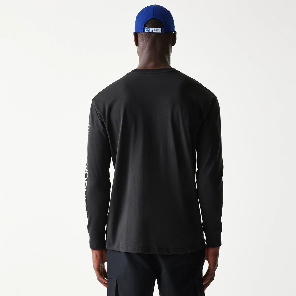 New Era LA Dodgers MLB Character Black Long Sleeve T-Shirt, rear view showing a plain back with white printed graphics down the right sleeve and a blue cap worn backwards with a raised logo on the cap's strap above the neck.