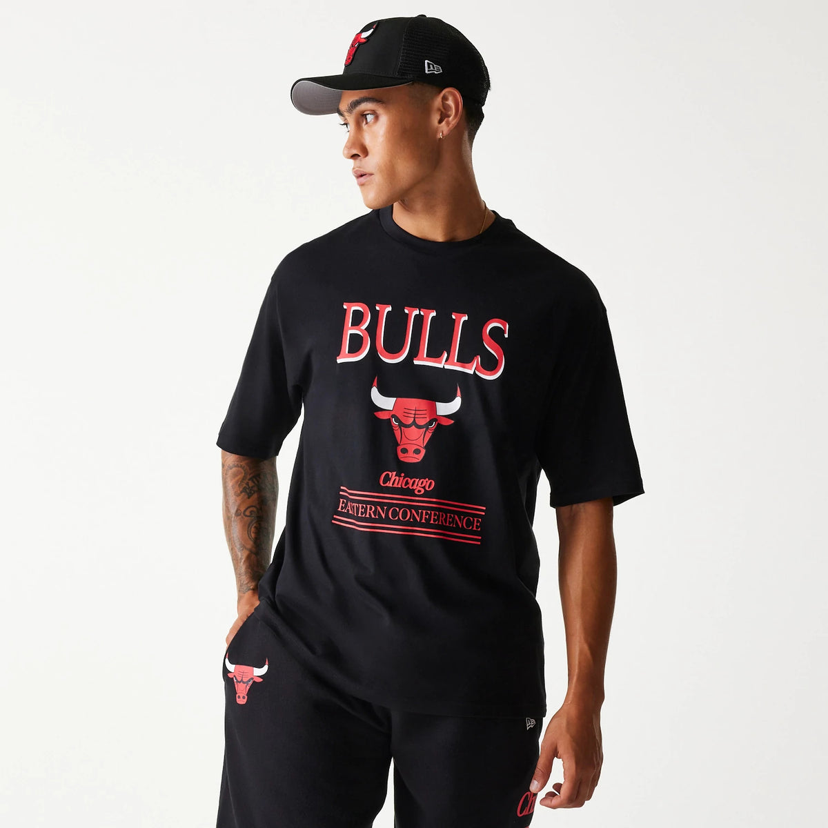 New Era Chicago Bulls NBA Team Graphic Black Oversized T-Shirt, on-model view showing a large front graphic with the Bulls logo and text in red and white, worn with matching black shorts featuring the same red Bulls logo on the left leg.