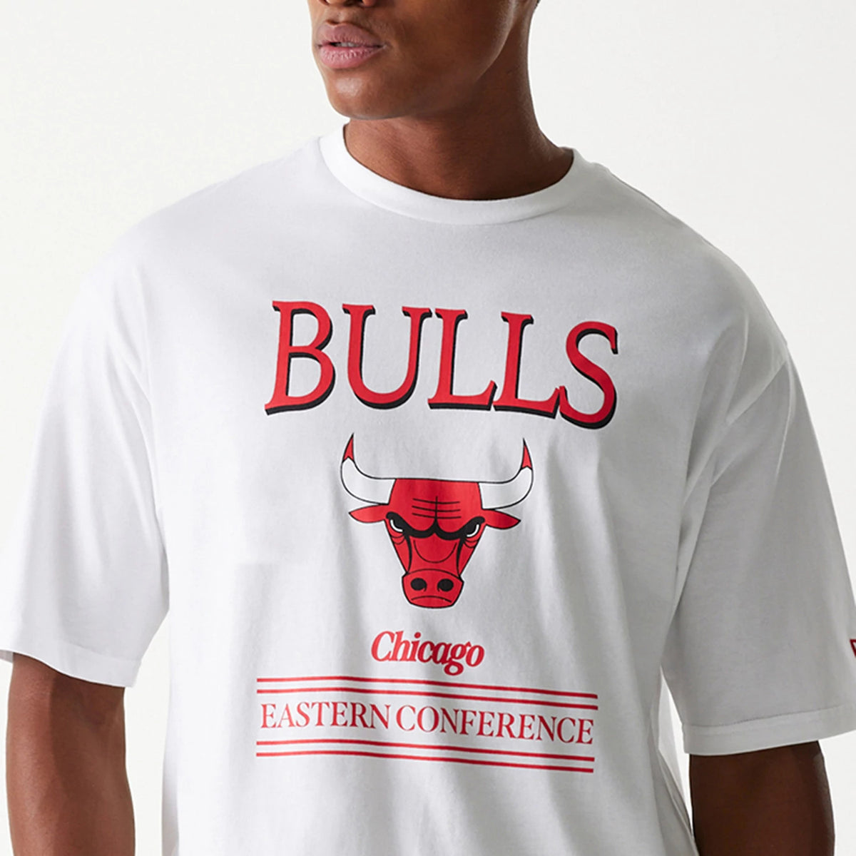 New Era Chicago Bulls NBA Team Graphic White Oversized T-Shirt, front view showing bold red BULLS text above a graphic of the red bull's head, with Chicago and Eastern Conference in red below on a white background.