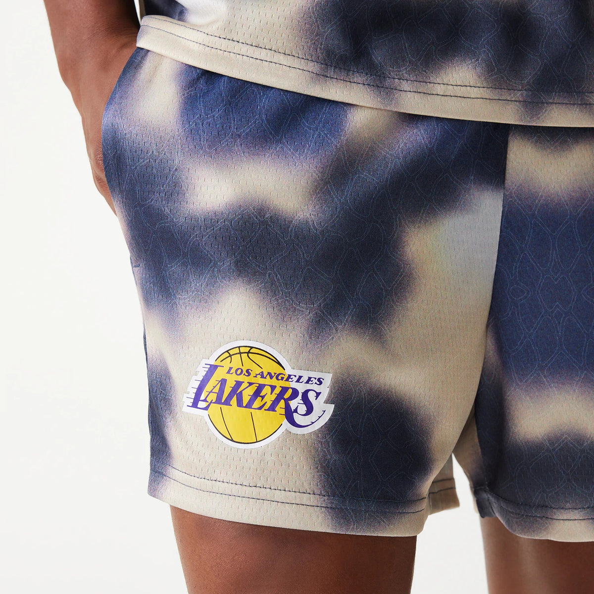 New Era LA Lakers NBA All Over Print Cream Shorts, side view showing a tie-dye pattern with the Los Angeles Lakers logo printed in yellow and purple on the left thigh near the hem.