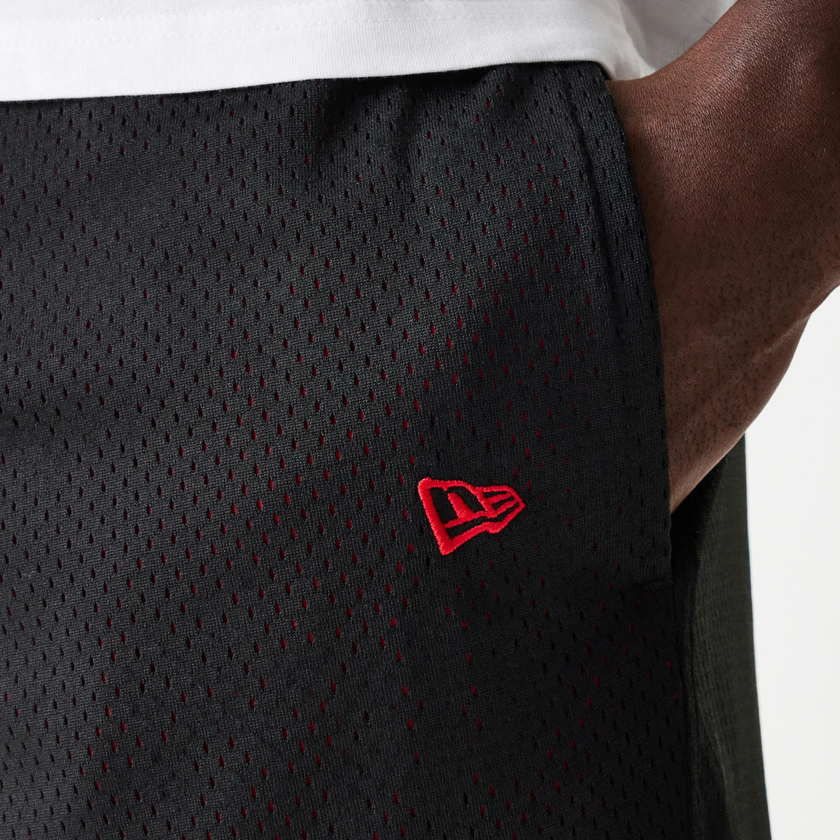 New Era Black Mesh Shorts, side view showing the textured black mesh fabric with small eyelets throughout and a raised red New Era logo positioned on the left leg near the seam.