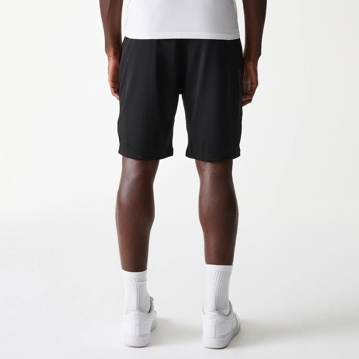 New Era Black Mesh Shorts, on-model view showing the rear of the black shorts with a straight hem just above the knee, worn with white socks and trainers, highlighting the relaxed fit and lightweight design.