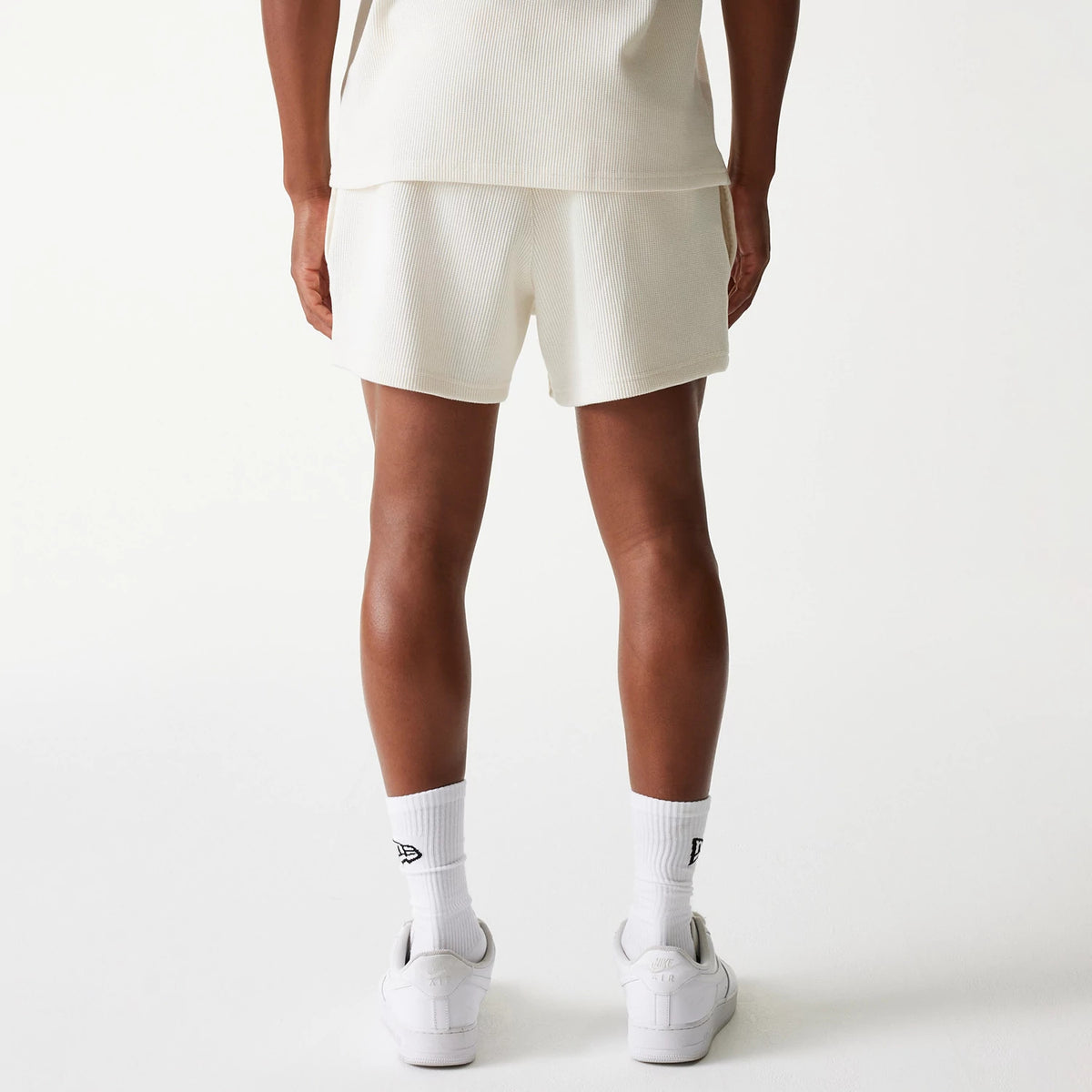 New Era Waffle Open White Shorts, rear view showing the shorts in an off-white hue with a straight cut above the knee, paired with matching socks featuring a debossed New Era logo on the side.