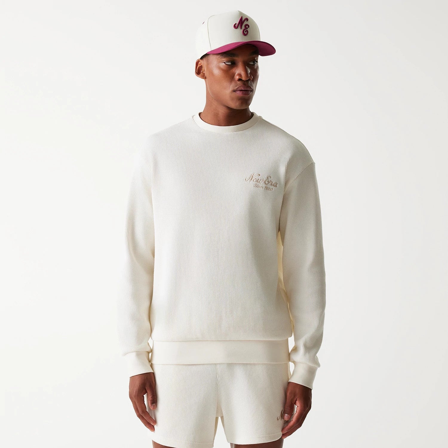 New Era Waffle Open White Oversized Crew Neck Sweater, on-model view styled with a white and burgundy cap, showing an embroidered logo on the left chest and ribbed texture throughout the body and sleeves.