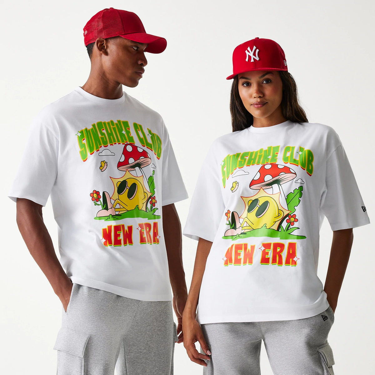 New Era Outdoor Graphic White Oversized T-Shirt, front view showing a colourful graphic with a smiling sun under a mushroom and text reading Sunshine Club above and New Era below, worn by two people wearing red caps.