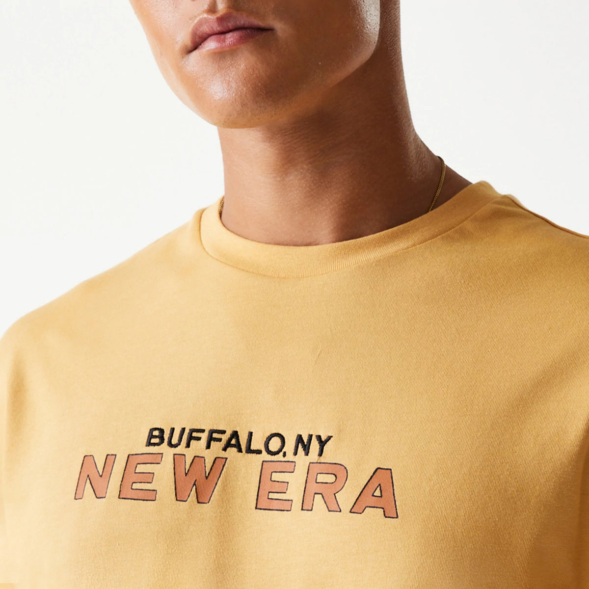 New Era Vacation Graphic Beige Oversized T-Shirt, front view showing the beige fabric with a printed BUFFALO, NY NEW ERA graphic in black and orange letters across the chest, on-model.