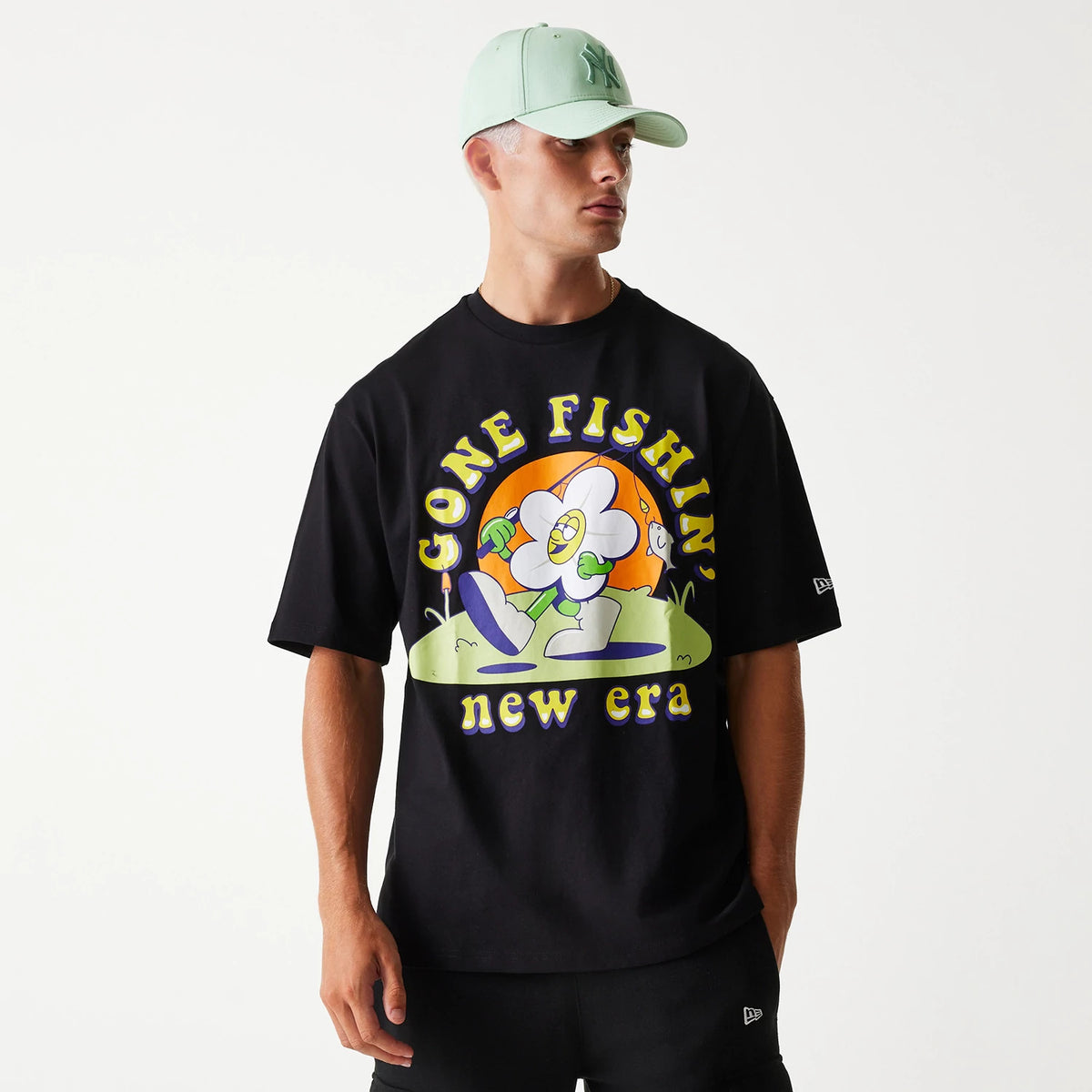 New Era Outdoor Graphic Black Oversized T-Shirt, on-model view showing a large colourful graphic on the front with text Gone Fishin' above a cartoon figure, and the New Era logo on the left sleeve.