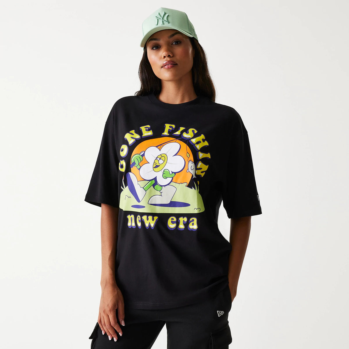 New Era Outdoor Graphic Black Oversized T-Shirt, front view showing a colourful cartoon graphic in the centre with Gone Fishin' text above and new era below, worn by a model wearing a green cap with a raised logo.