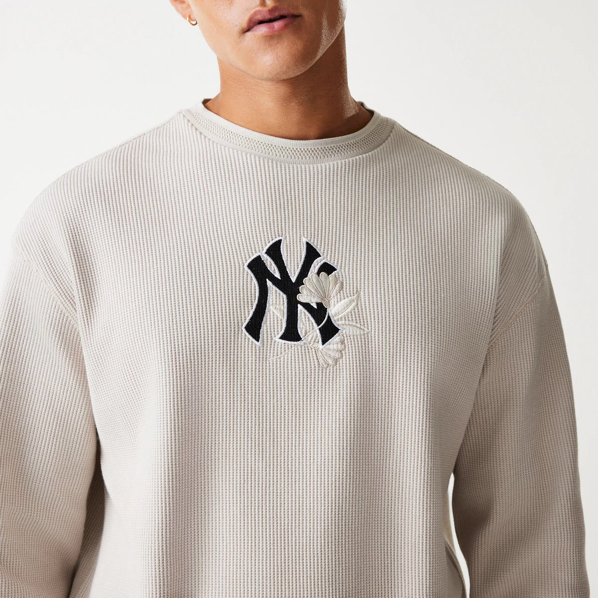 New Era New York Yankees MLB Waffle Cream Oversized Crew Neck Sweater, front view on a model showing the black NY logo with white floral embroidery on the textured cream fabric, with a ribbed collar edge.