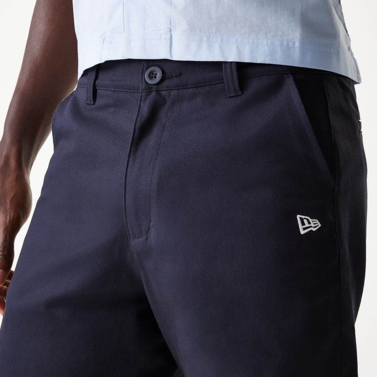 New Era Navy Chino Shorts, side view showing a close-up of the navy fabric with a raised white New Era logo on the pocket, belt loops and a button and zip fastening at the waist.