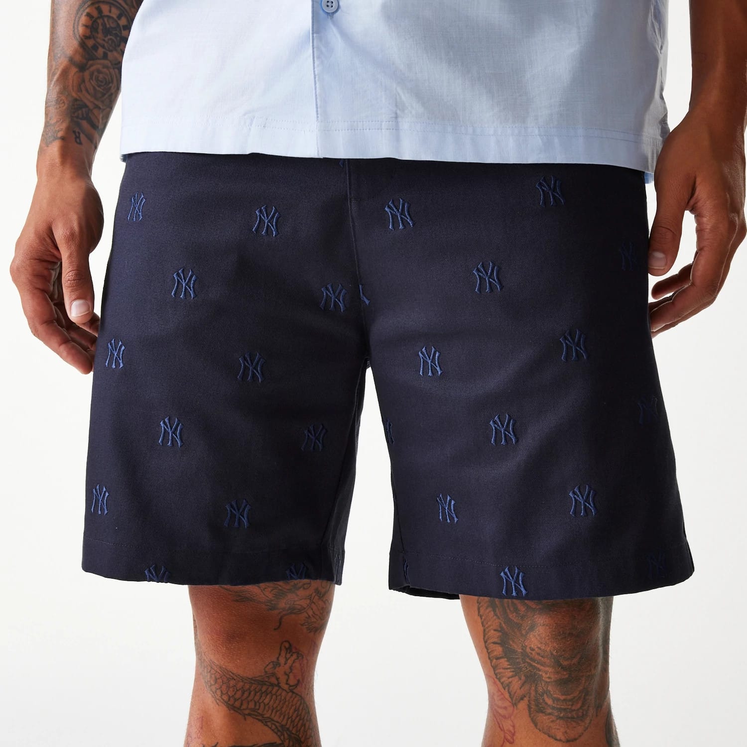 New Era New York Yankees MLB Monogram Navy Shorts, on-model view showing the knee-length navy shorts with embroidered New York Yankees logos scattered across, and the model's hands resting at their sides against a plain white background.
