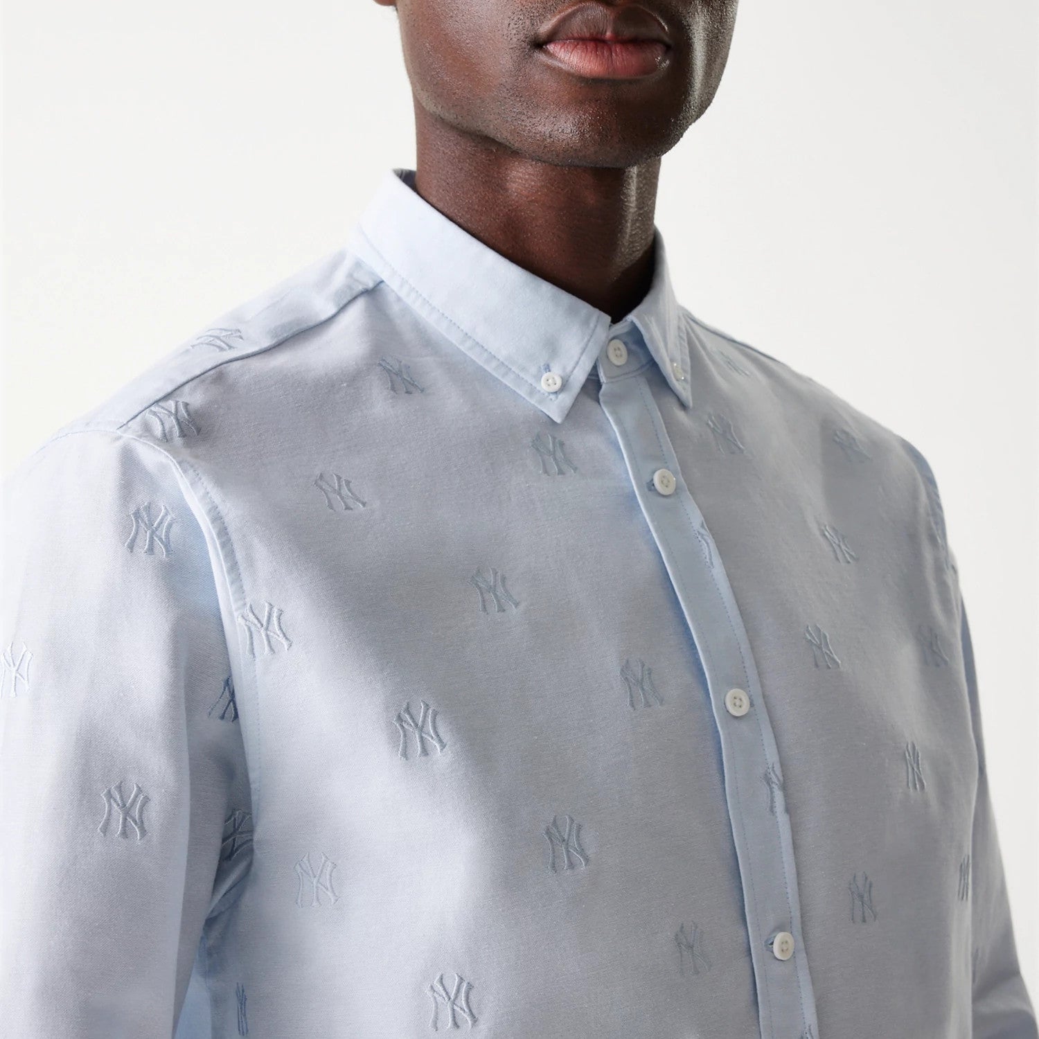 New Era New York Yankees MLB Monogram Pastel Blue Long Sleeve Shirt, close-up on a model showing the embroidered NY logos across the light blue fabric, with a button-down collar and white buttons lining the front placket.