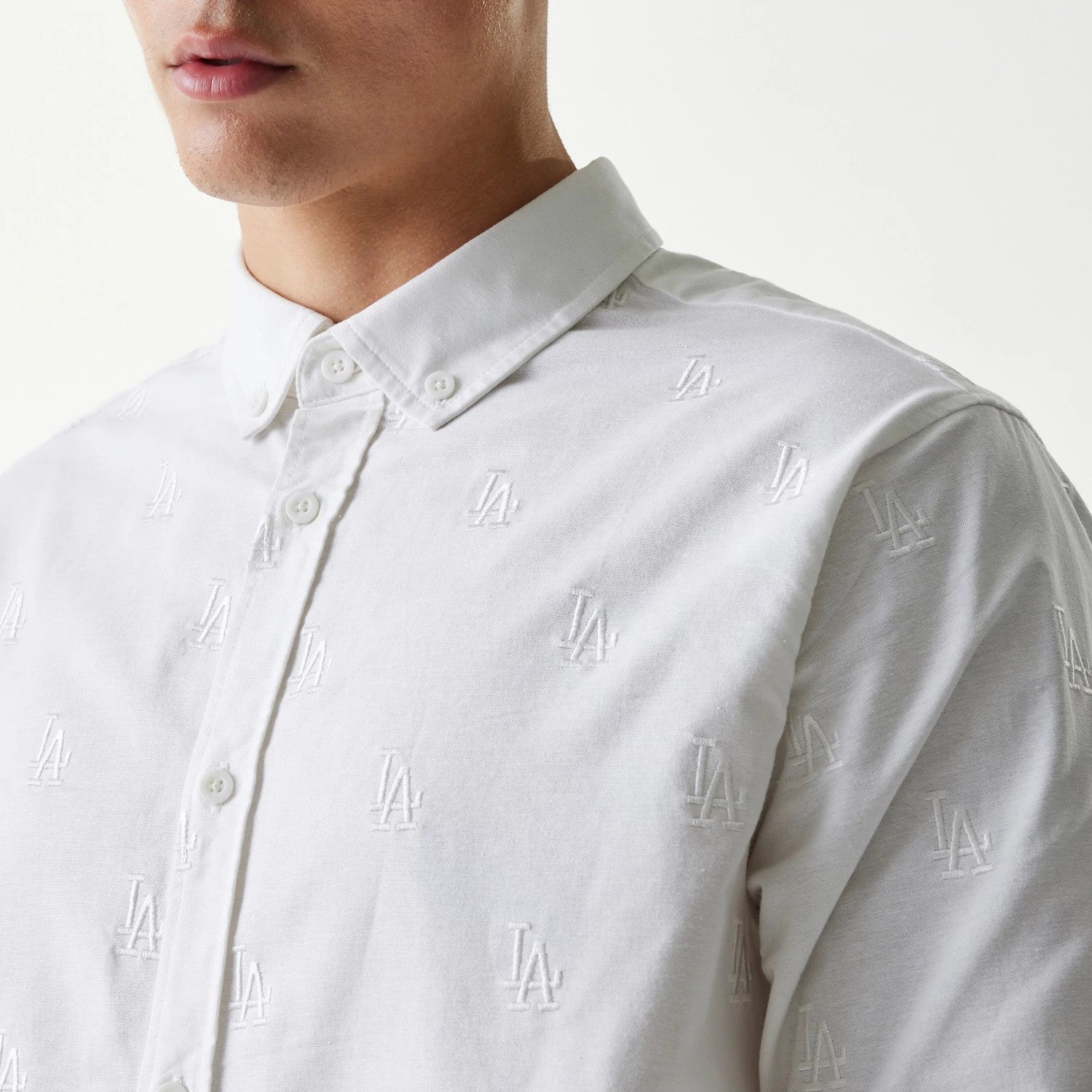 New Era LA Dodgers MLB Monogram White Long Sleeve Shirt, three-quarter view on a model showing white LA monogram embroidery across the front on a clean white background with white buttons on the collar and placket.