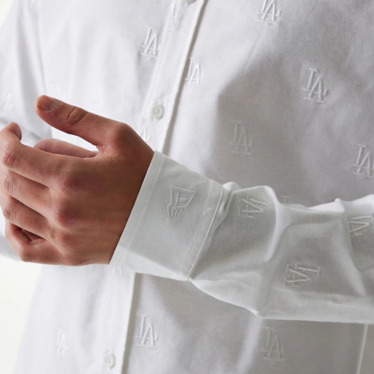 New Era LA Dodgers MLB Monogram White Long Sleeve Shirt, close-up showing white embroidered LA logos across the fabric, with a focus on the sleeve featuring the New Era flag logo near the cuff.