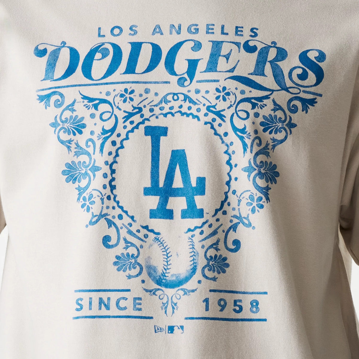 New Era LA Dodgers MLB Floral Graphic Cream Oversized T-Shirt, front view showing a large blue graphic design with LOS ANGELES DODGERS text, a central LA logo, ornate floral patterns, and SINCE 1958 below on the cream fabric.