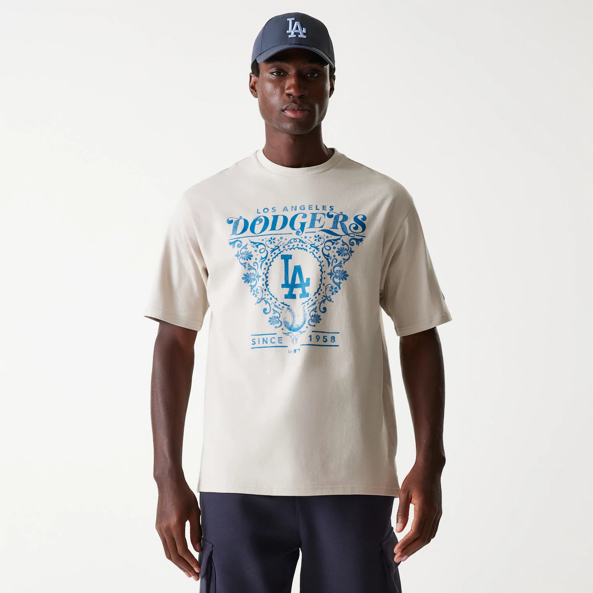 New Era LA Dodgers MLB Floral Graphic Cream Oversized T-Shirt, on-model view showing the blue floral graphic with Los Angeles Dodgers text on the front, and a matching cap with an embroidered LA logo worn on the head.