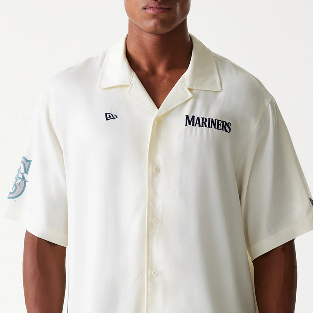 New Era Seattle Mariners MLB Graphic Open White Revere Short Sleeve Shirt, front view on a model featuring navy Mariners lettering on the left chest, a New Era flag logo on the right chest, and a teal Mariners logo on the left sleeve.
