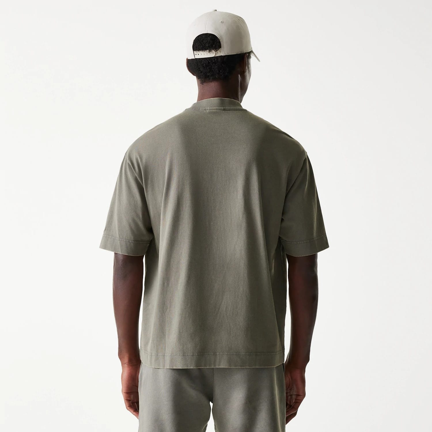 New Era LA Lakers NBA Washed Grey Box T-Shirt, rear view showing the plain grey back of the boxy t-shirt, short sleeves slightly extending over the shoulders, and a cream cap on a person, featuring a row of eyelets on the cap.
