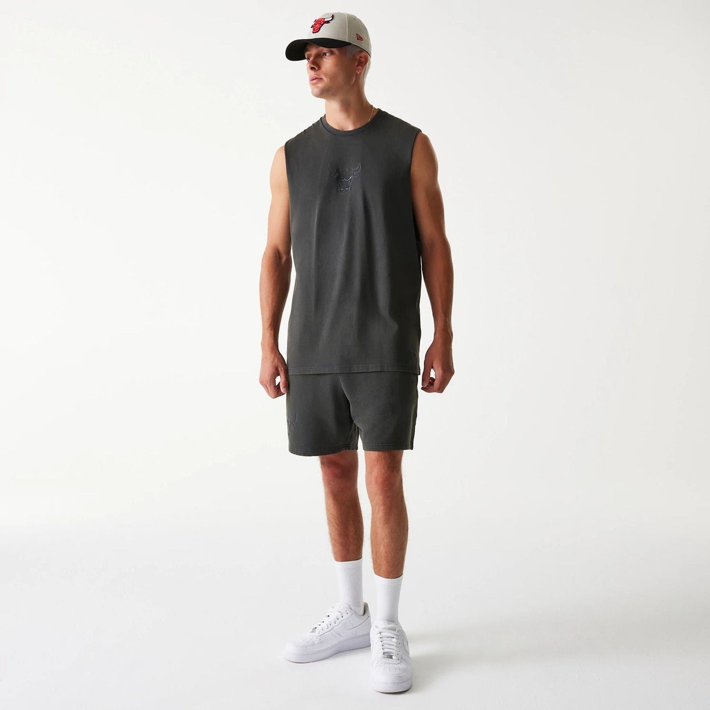New Era Chicago Bulls NBA Washed Grey Shorts, on-model view showing the grey shorts worn with a matching sleeveless top, featuring an embossed Chicago Bulls logo on the left leg and complemented by a grey cap with a Bulls emblem.