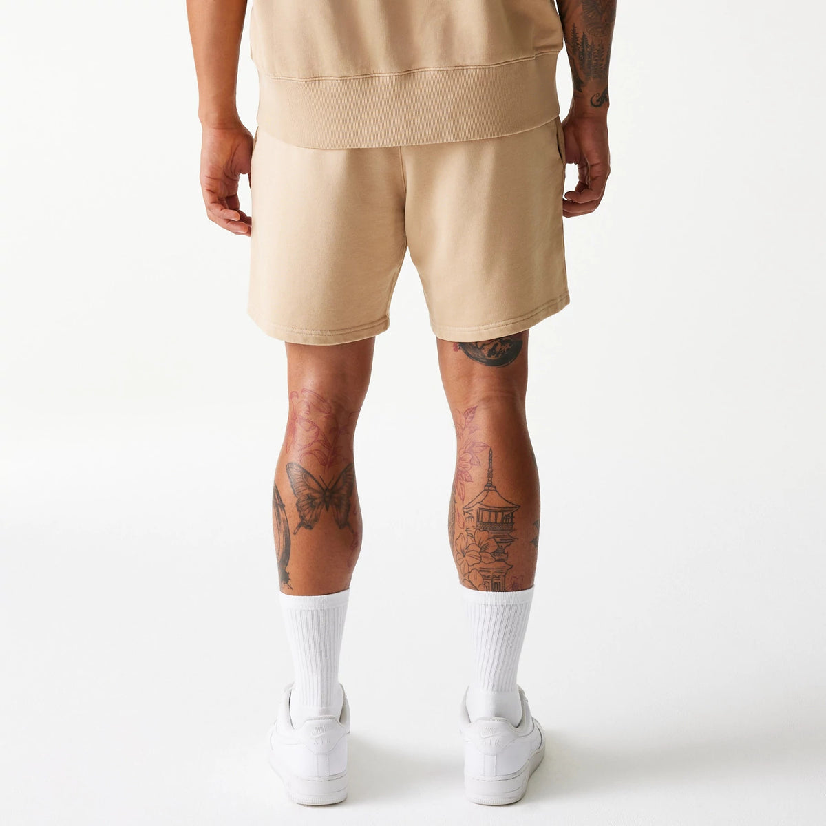 New Era Chicago Bulls NBA Washed Beige Shorts, rear view showing the soft beige colour and relaxed fit, with a straight hem falling above the knee, worn with white socks and trainers against a plain background.