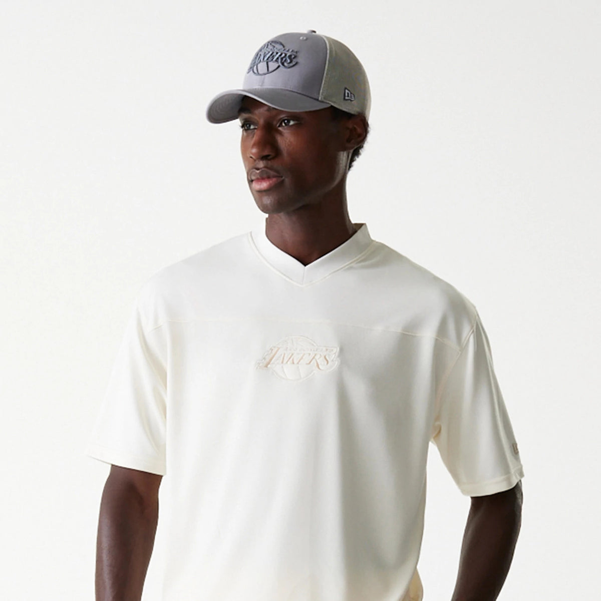 New Era LA Lakers NBA Tonal Open White Mesh Jersey, on a model pairing it with a grey cap, showing the embroidered Lakers logo on the chest and tonal white mesh fabric, capturing a casual and sports-inspired look.