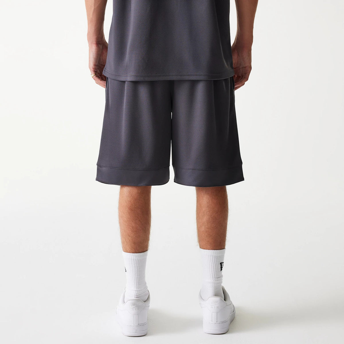 New Era Chicago Bulls NBA Tonal Dark Grey Mesh Shorts, rear view showing the dark grey mesh fabric with a loose fit above the knee and an elasticated waistband, styled with white socks and white trainers.