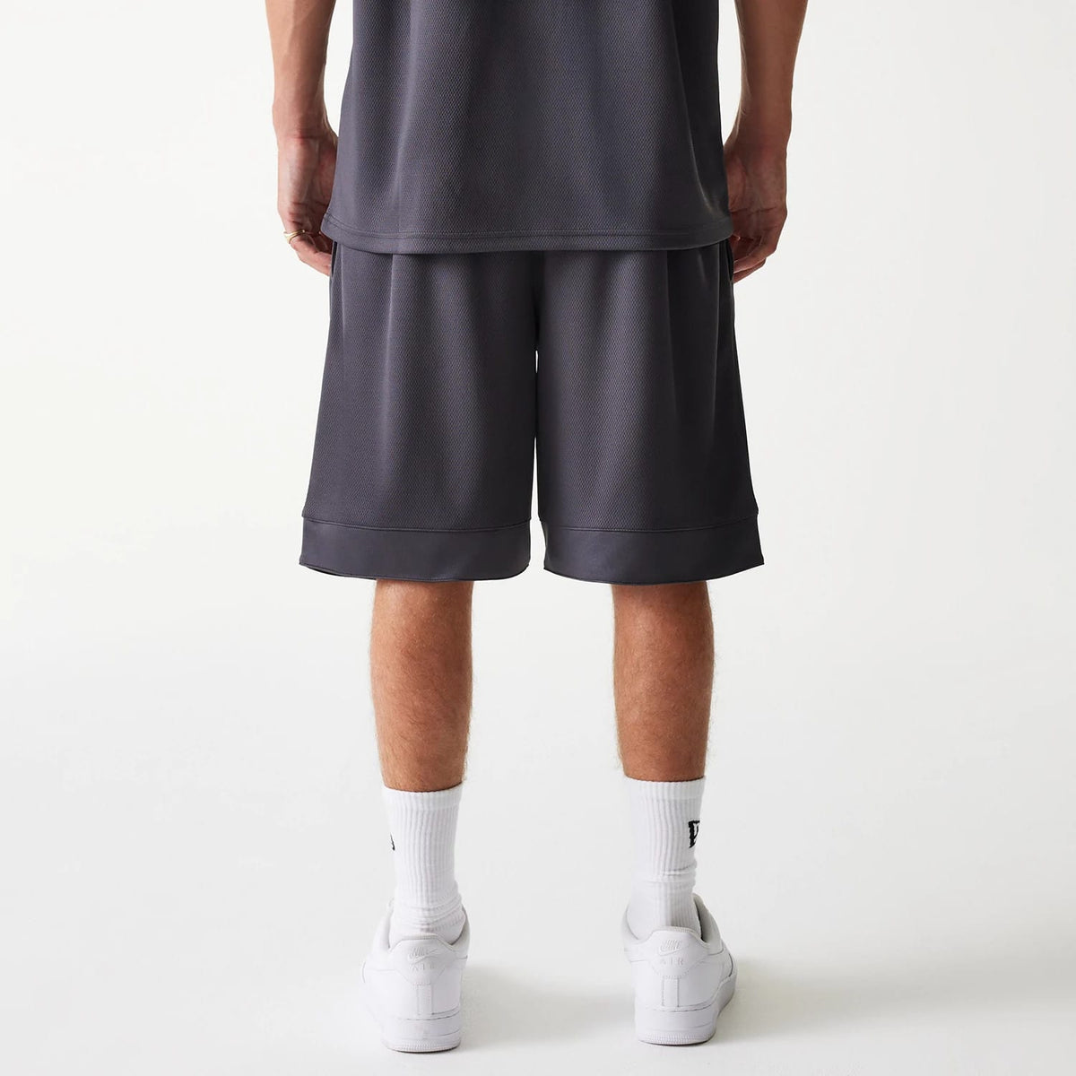 New Era Chicago Bulls NBA Tonal Dark Grey Mesh Shorts, rear view showing the dark grey mesh fabric with a loose fit above the knee and an elasticated waistband, styled with white socks and white trainers.