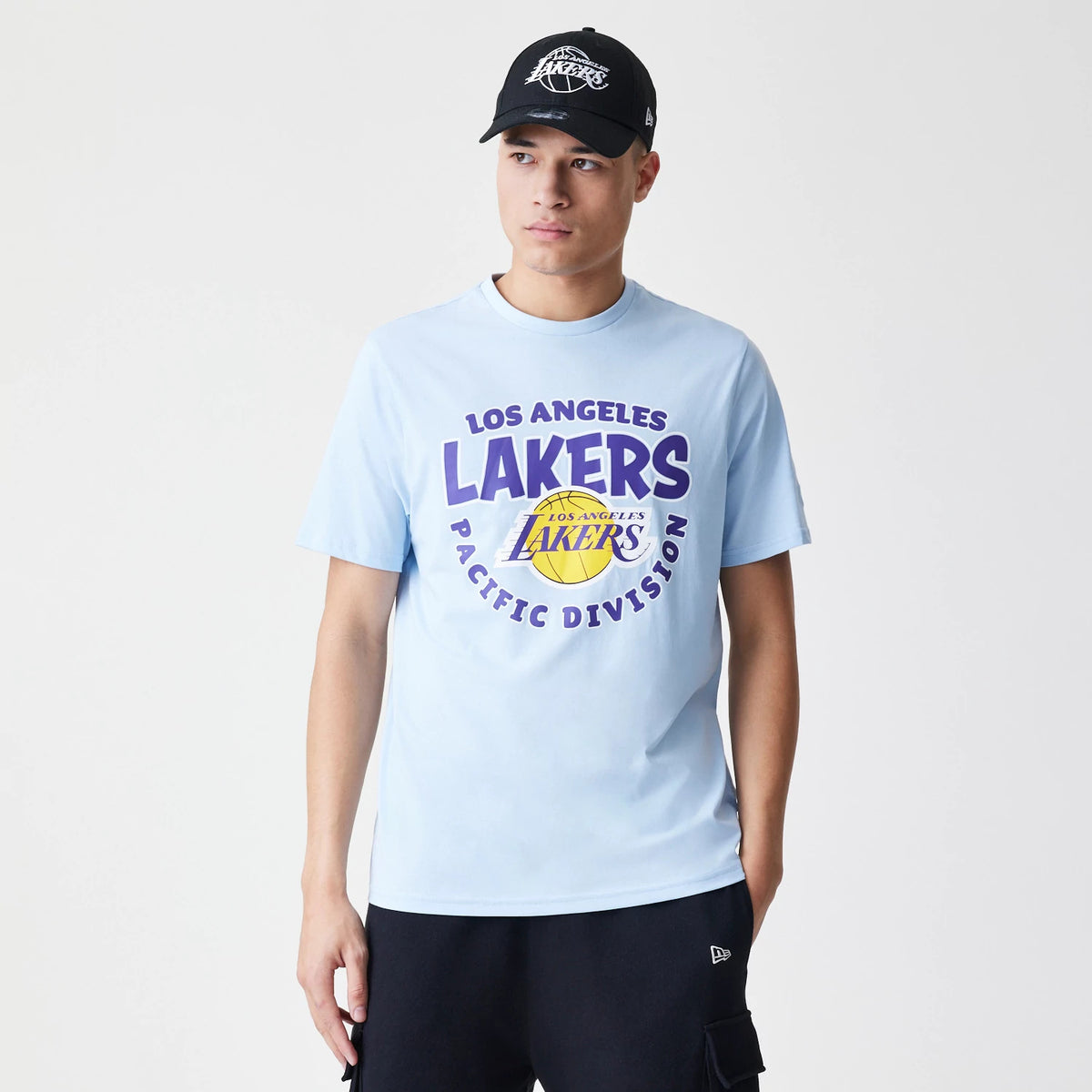 New Era LA Lakers NBA Bubble Wordmark Pastel Blue T-Shirt, on-model view showing the pastel blue colour with a large front print of the Los Angeles Lakers logo in purple and yellow, paired with a black cap featuring a debossed Lakers logo.