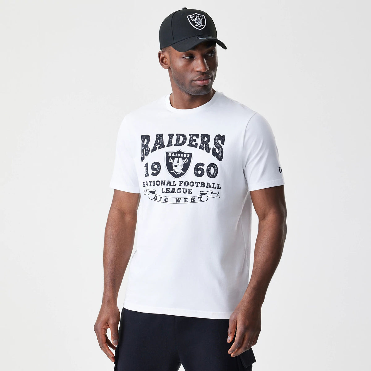 New Era Las Vegas Raiders NFL Stack Arch Logo White T-Shirt, on-model view featuring a bold black Raiders graphic across the chest, a small debossed New Era logo on the left sleeve, paired with a black cap displaying an embroidered Raiders logo on the front.