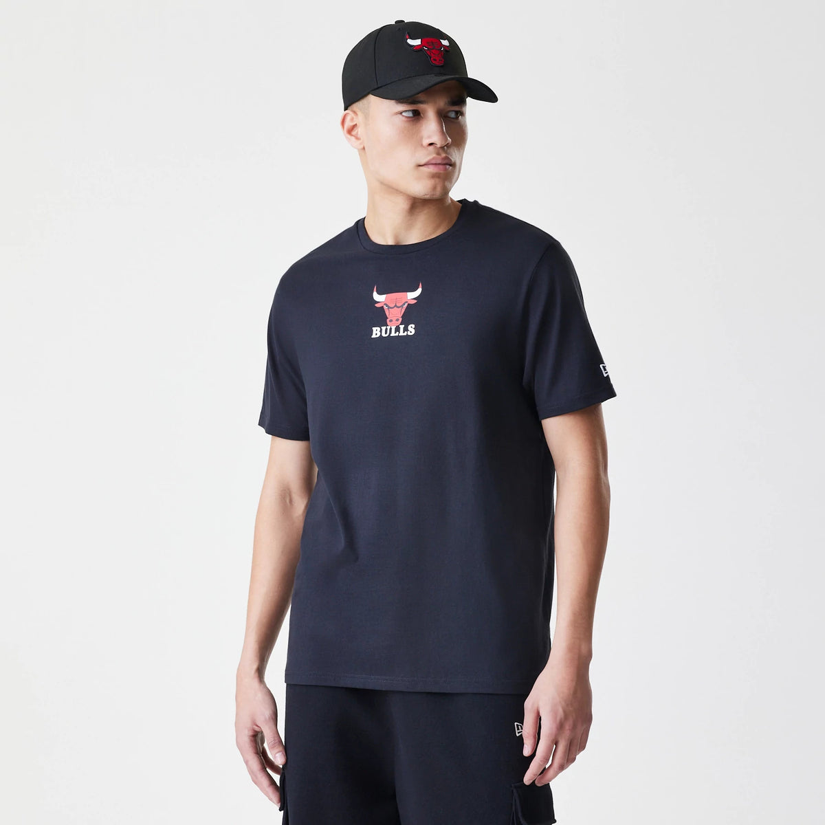 New Era Chicago Bulls NBA Logo Black T-Shirt, on-model view showing a red and white Chicago Bulls logo centred on the chest, an embroidered New Era logo on the left sleeve, worn with a matching black cap featuring a raised Bulls logo.