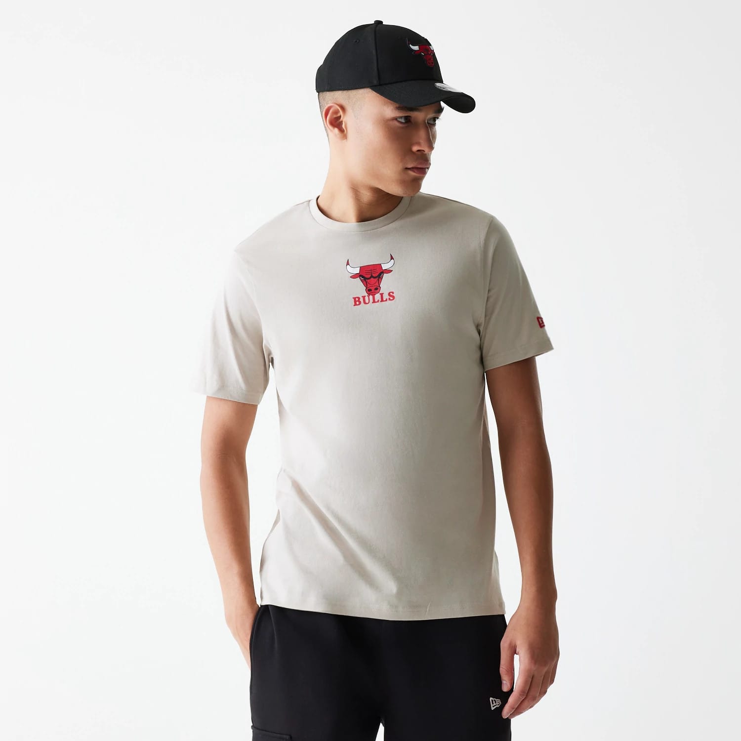 New Era Chicago Bulls NBA Logo Cream T-Shirt, on-model view showing the red Bulls logo printed at the centre of the chest, a small red logo on the left sleeve, paired with black shorts and a black cap featuring a raised Bulls logo.