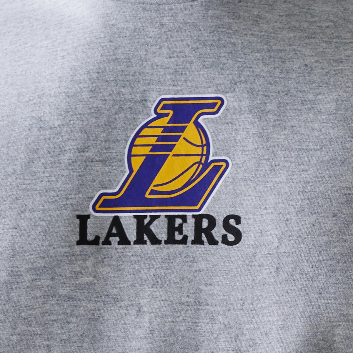 New Era LA Lakers NBA Logo Grey T-Shirt, front view displaying a large yellow and purple embroidered Lakers logo with a basketball illustration at the centre of the chest on a light grey fabric.