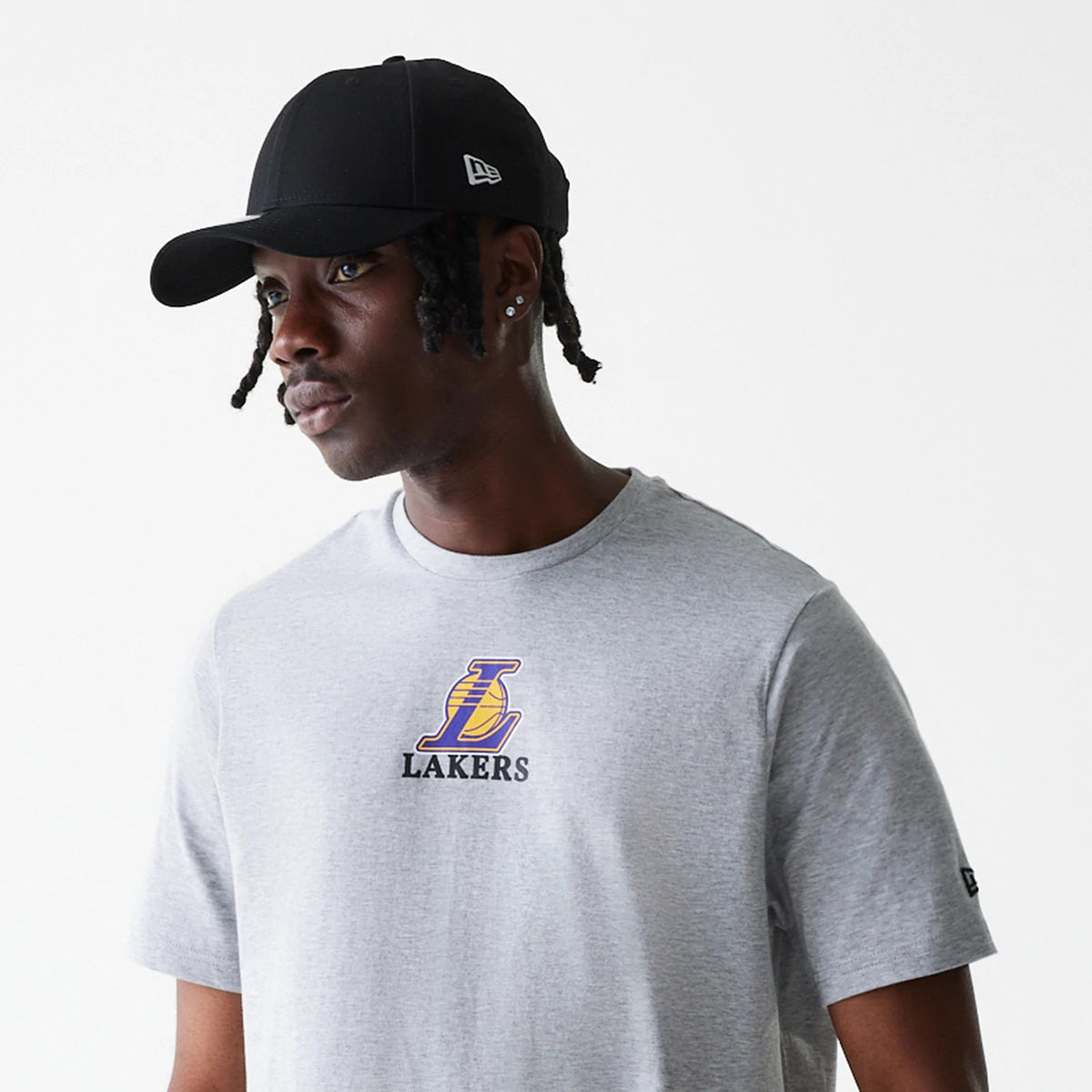 New Era LA Lakers NBA Logo Grey T-Shirt, on-model view showing a grey T-shirt with the LA Lakers logo in purple and yellow on the front chest, paired with a black cap featuring a raised New Era logo on the side.