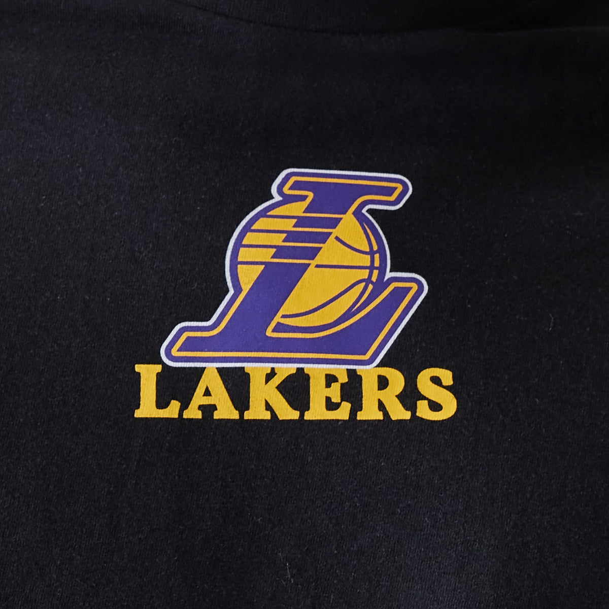 New Era LA Lakers NBA Logo Black T-Shirt, front view featuring the large purple and gold Lakers logo printed at the centre of the chest on a black fabric backdrop.