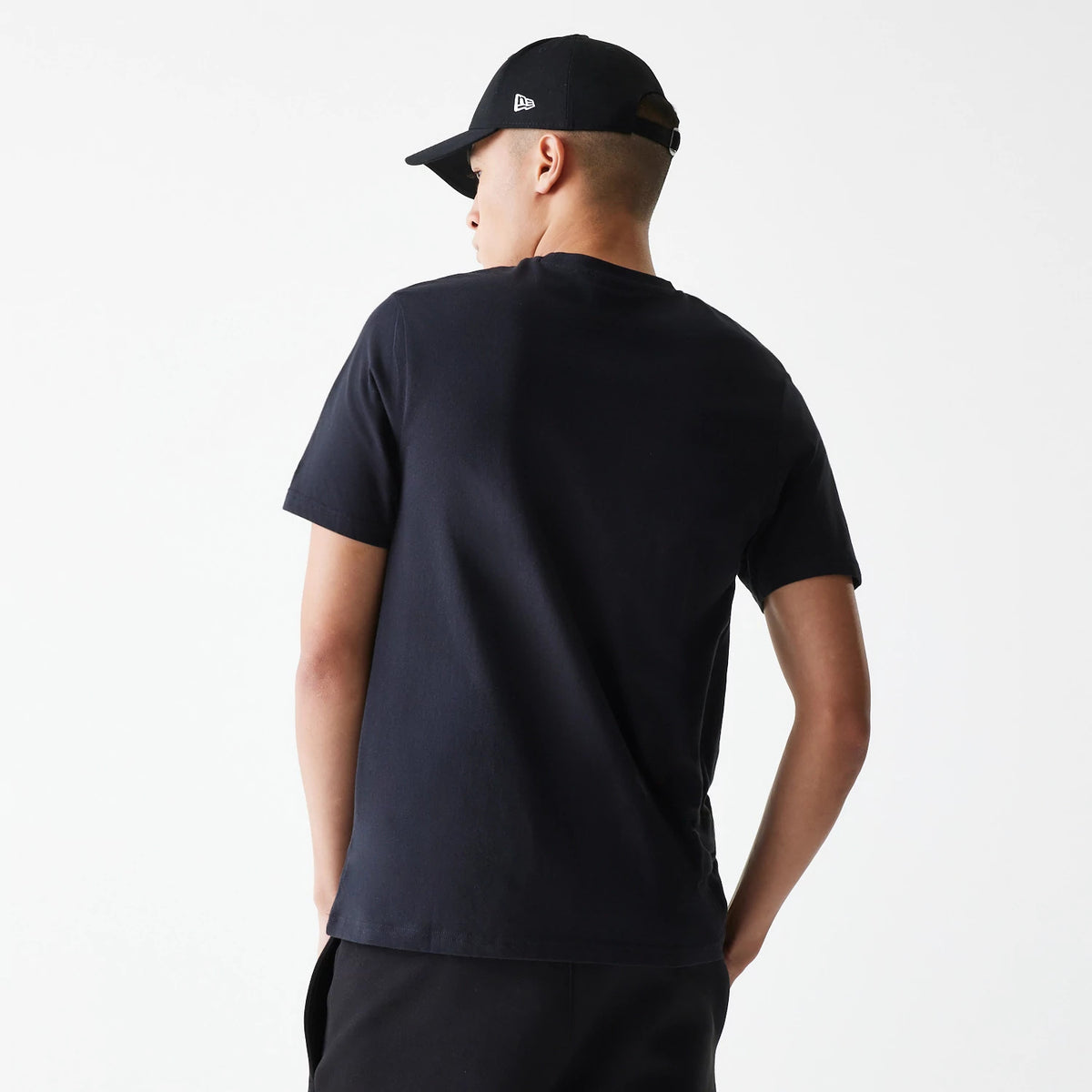 New Era LA Lakers NBA Logo Black T-Shirt, rear view showing the plain black back with short sleeves and a person wearing a black New Era cap with a white debossed logo on the side.