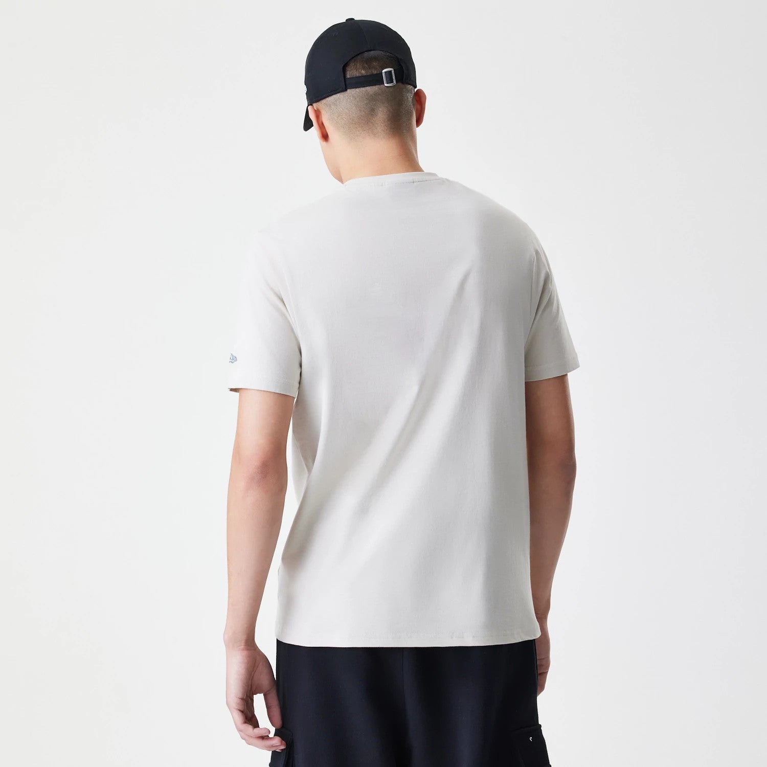 New Era Burger Graphic Cream T-Shirt, rear view showing the plain cream back of the T-shirt with short sleeves, a small raised logo on the left sleeve and a black cap worn by the person modeling the shirt.