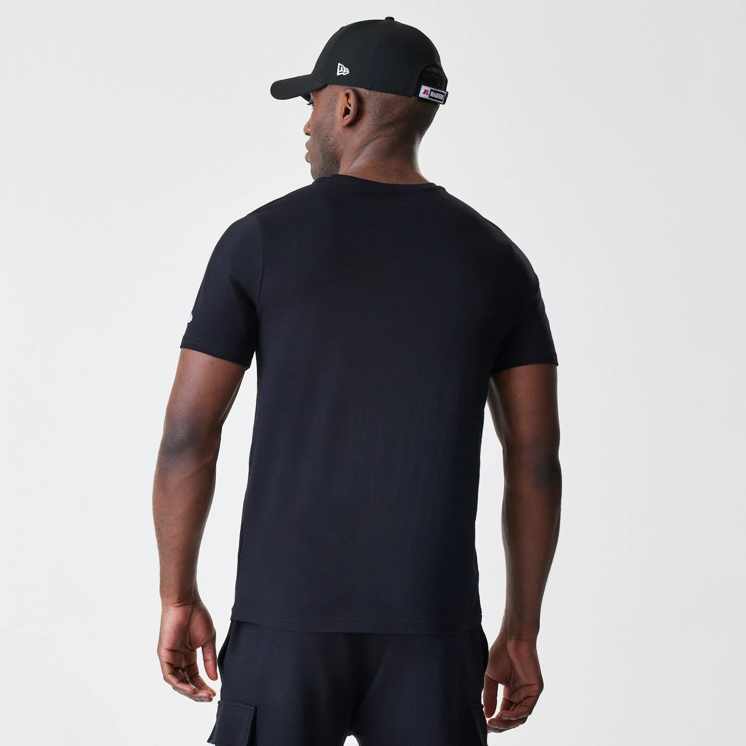 New Era Las Vegas Raiders NFL Logo Black T-Shirt, rear view showing plain black back panel with a small debossed logo on the left sleeve, worn by a model in a black cap with a debossed logo on the side.