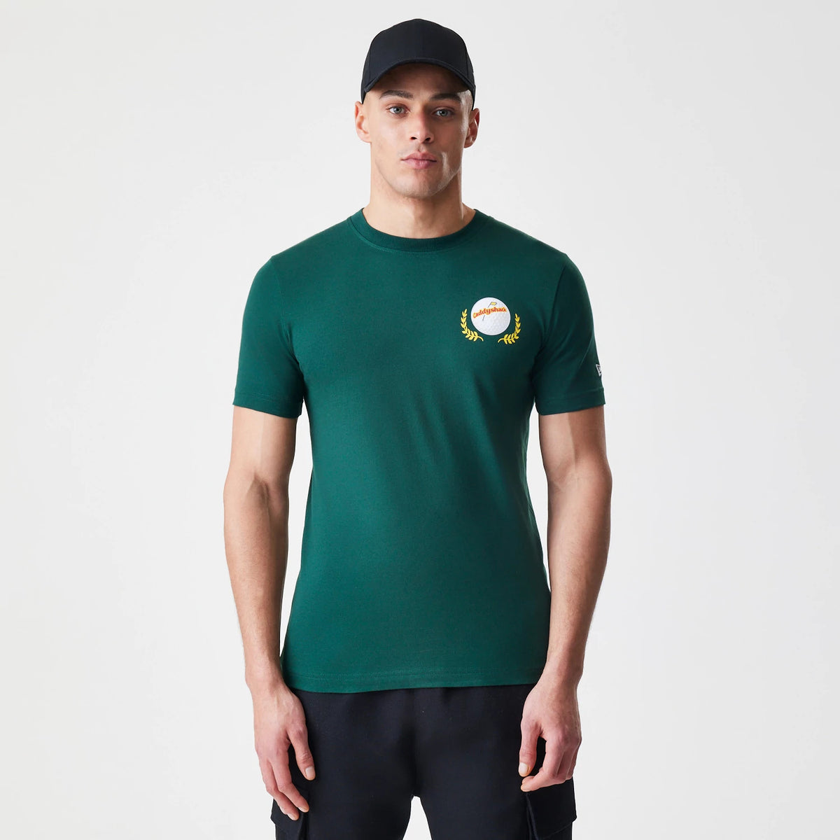 New Era Caddyshack It's In The Hole Dark Green T-Shirt, on-model view showing a dark green T-shirt with a circular emblem on the left chest and a small raised logo on the left sleeve.