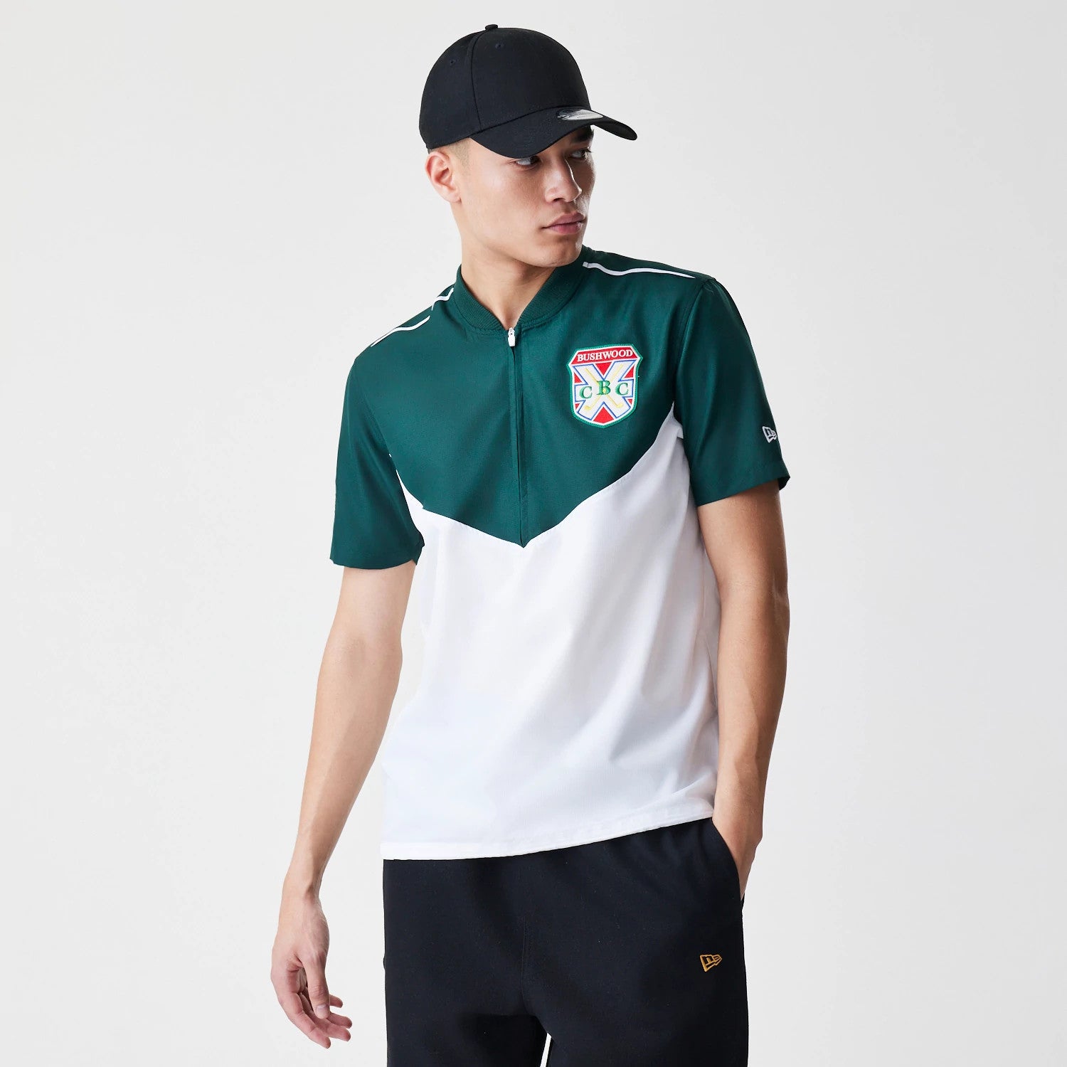 New Era Caddyshack BushWood White 1/4 Zip Polo T-Shirt, on-model view showing the green and white polo with a quarter zip and BushWood crest on the chest, the New Era logo debossed on the left sleeve and a black cap worn by the model.