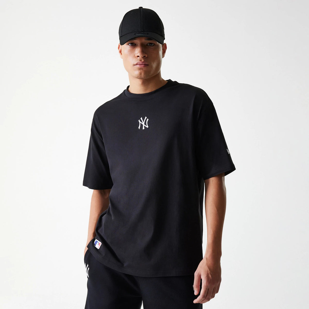 New Era New York Yankees MLB League Essential Black Oversized T-Shirt, front view showing a white embroidered New York Yankees logo centred on the chest, worn by a model with short sleeves and loose fit design.