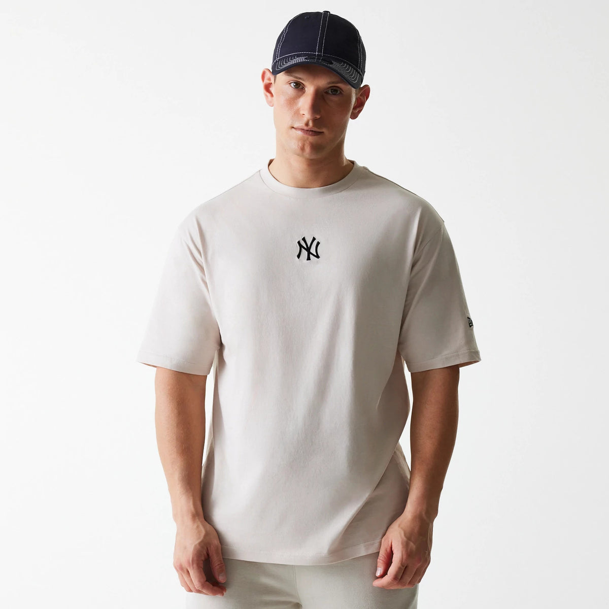 New Era New York Yankees MLB League Essential Cream Oversized T-Shirt, on-model view showing a cream oversized fit with a black embroidered NY logo on the chest and a small debossed New Era logo on the left sleeve.