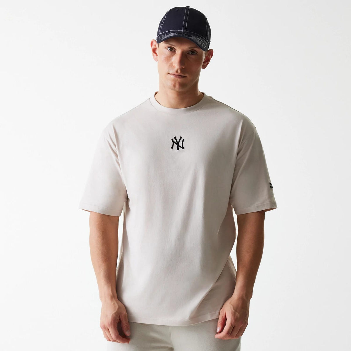 New Era New York Yankees MLB League Essential Cream Oversized T-Shirt, on-model view showing a cream oversized fit with a black embroidered NY logo on the chest and a small debossed New Era logo on the left sleeve.