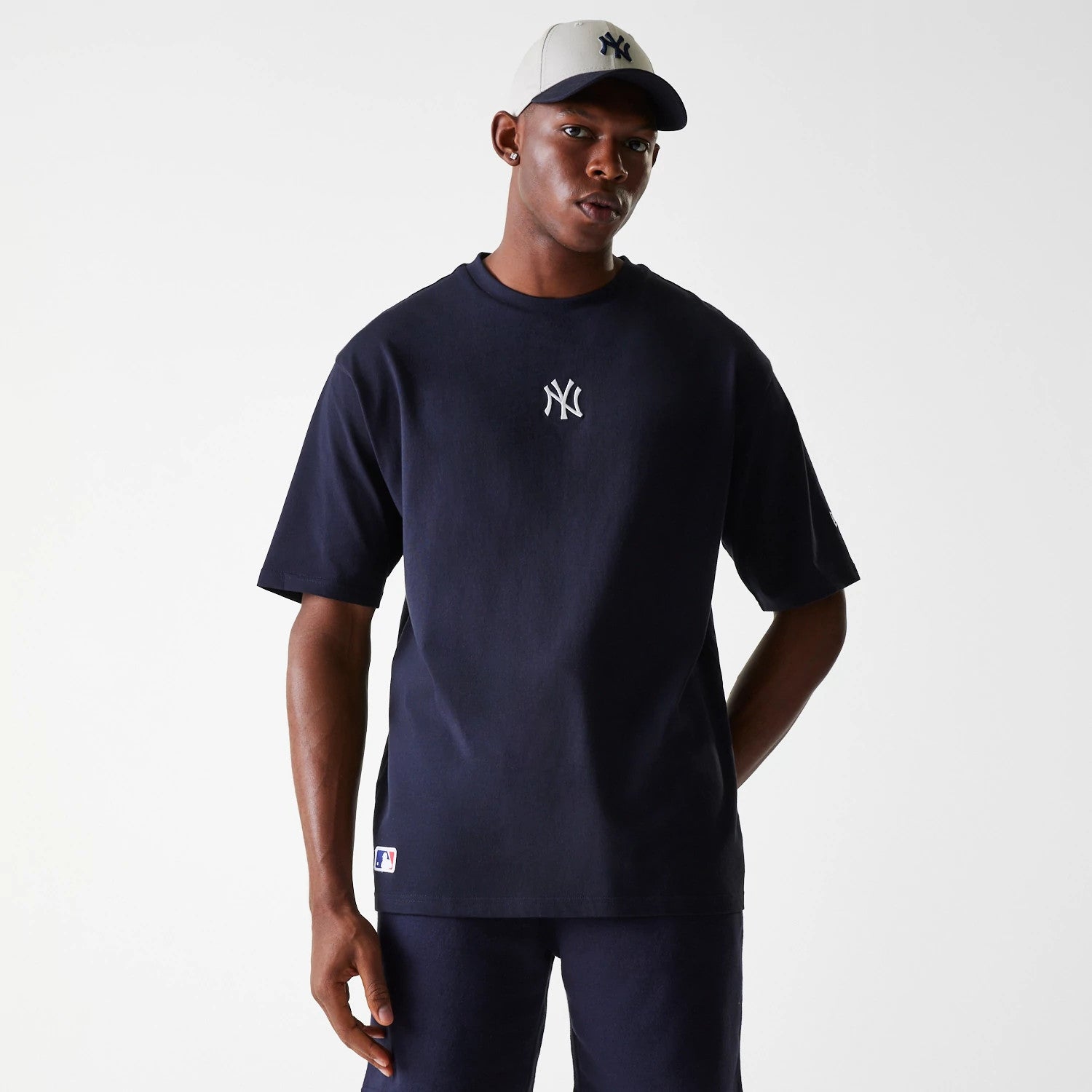 New Era New York Yankees MLB League Essential Navy Oversized T-Shirt, front view showing a white New York Yankees logo centred on the chest, short sleeves, and a relaxed fit, worn by a model wearing a navy and cream baseball cap.
