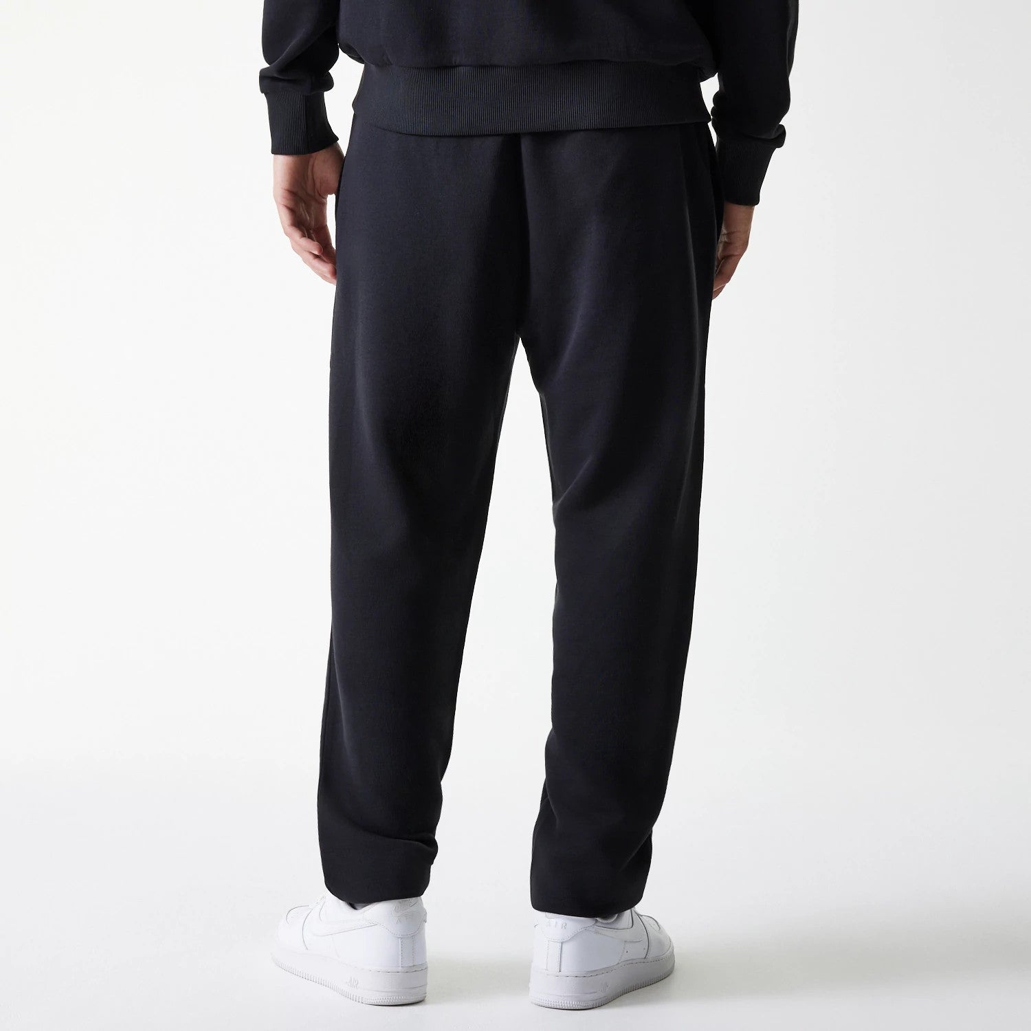 New Era New York Yankees MLB League Essential Midi French Terry Black Joggers, back view on a model showing the ribbed waistband and cuffed ankles, with a relaxed fit and soft fabric drape over white trainers.