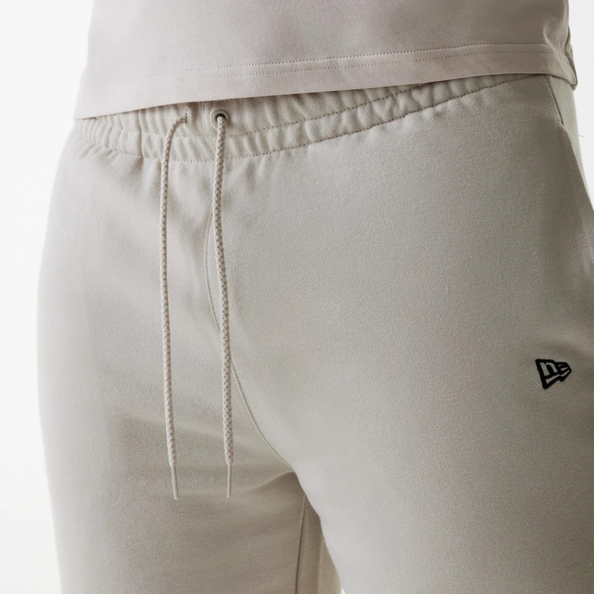 New Era New York Yankees MLB League Essential French Terry Cream Shorts, side view showing the cream fabric with elastic waistband, cream drawstrings hanging at the front, and a black embroidered New Era logo near the left pocket.