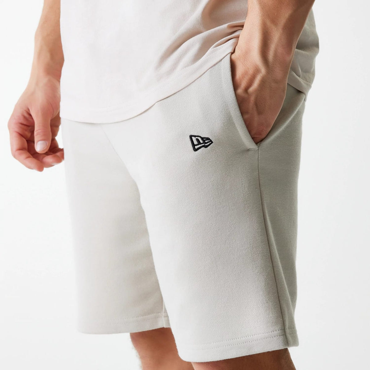 New Era New York Yankees MLB League Essential French Terry Cream Shorts, side view showing the cream colour with a black embroidered New Era logo on the upper left thigh near the pocket, and the shorts falling just above the knee.