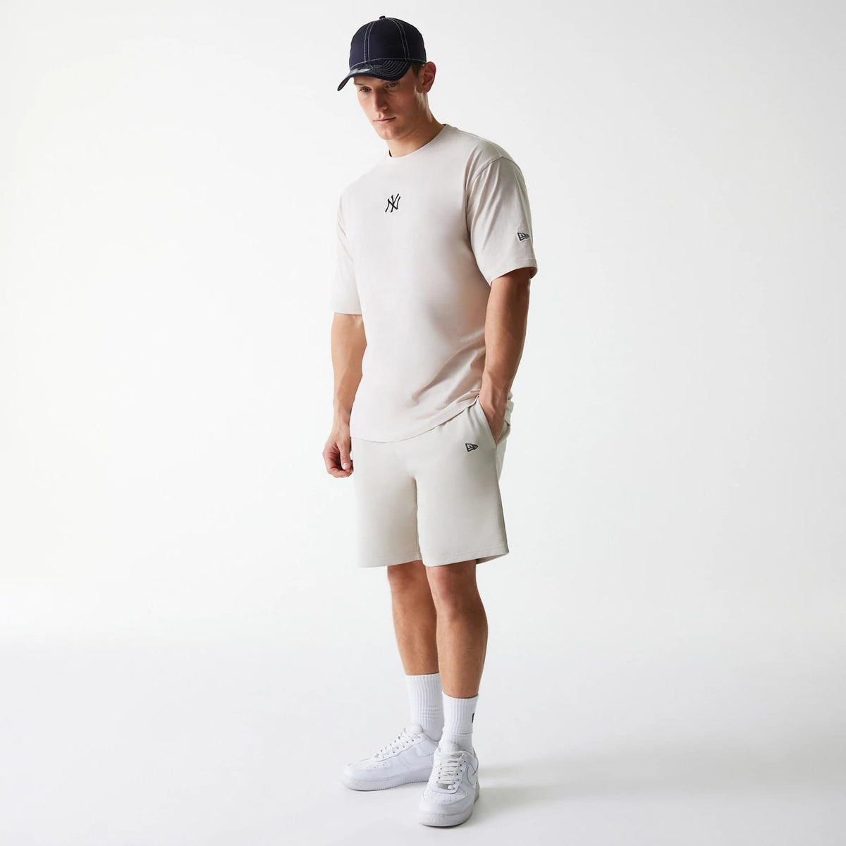 New Era New York Yankees MLB League Essential French Terry Cream Shorts, on-model view showing cream shorts with pockets, a raised New Era logo on the left leg, paired with a matching cream t-shirt featuring a New York Yankees emblem.